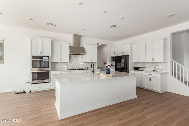 kitchen featuring fridge, visible vents, a sink, double oven, and wall chimney range hood