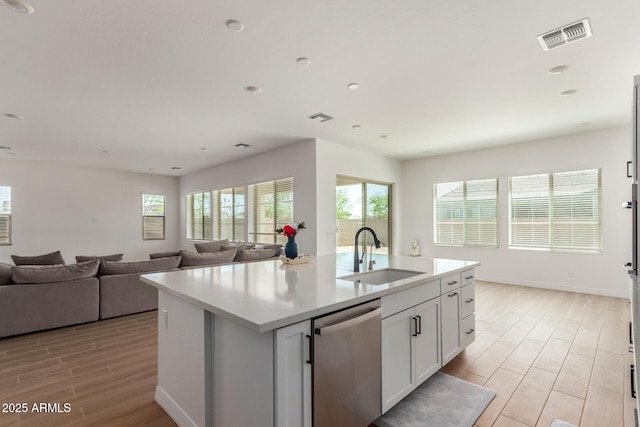 kitchen featuring visible vents, wood finish floors, an island with sink, a sink, and dishwasher