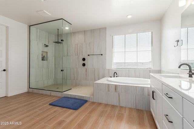 bathroom with wood finish floors, tiled shower, a bath, and vanity