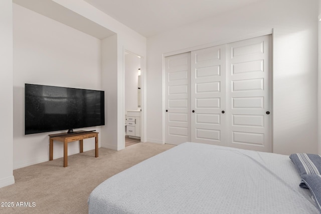 bedroom with light colored carpet, a closet, ensuite bathroom, and baseboards