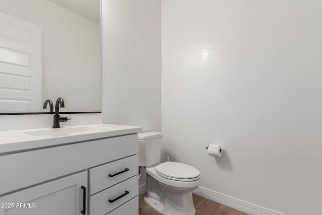 half bath with toilet, vanity, baseboards, and wood finished floors