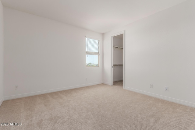 unfurnished bedroom featuring baseboards, light carpet, and a spacious closet