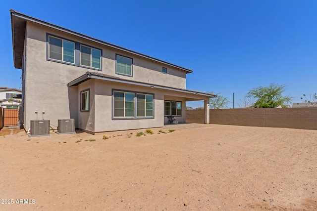 rear view of house featuring stucco siding, central AC unit, and a fenced backyard