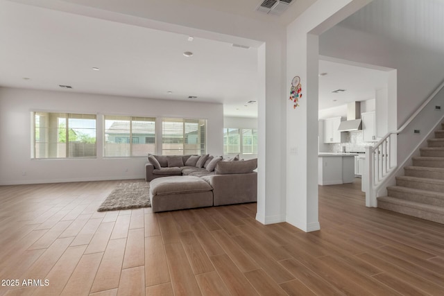 living room featuring light wood finished floors, visible vents, stairs, and a wealth of natural light