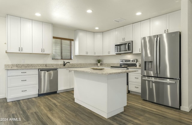 kitchen with stainless steel appliances, a kitchen island, light stone counters, dark hardwood / wood-style floors, and white cabinets