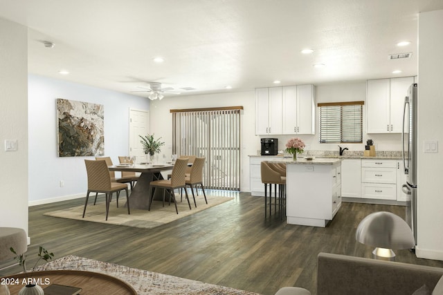 kitchen featuring dark wood-type flooring, white cabinets, a kitchen breakfast bar, ceiling fan, and light stone counters