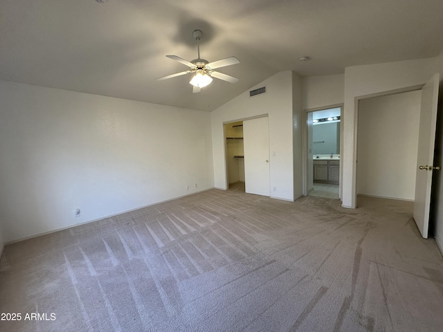 unfurnished bedroom featuring lofted ceiling, light colored carpet, visible vents, a ceiling fan, and ensuite bath