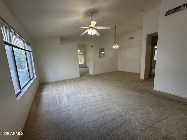 carpeted spare room with lofted ceiling, ceiling fan with notable chandelier, and visible vents