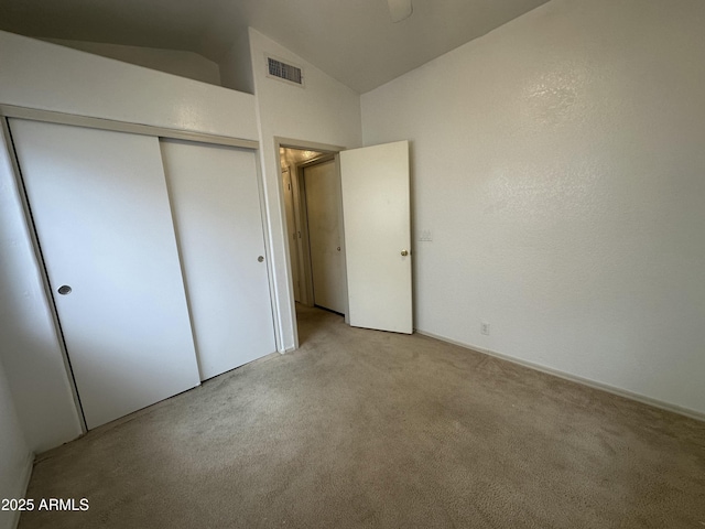 unfurnished bedroom featuring light carpet, vaulted ceiling, a closet, and visible vents