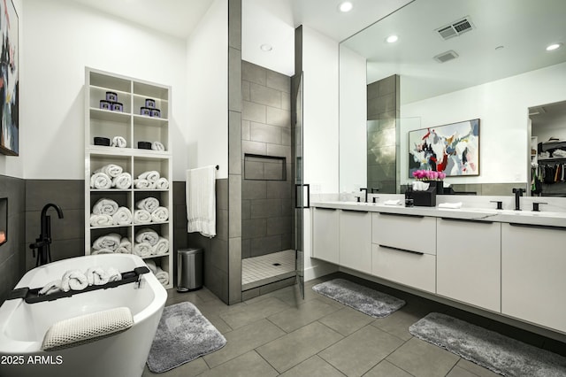 bathroom with double vanity, visible vents, a soaking tub, a shower stall, and a sink