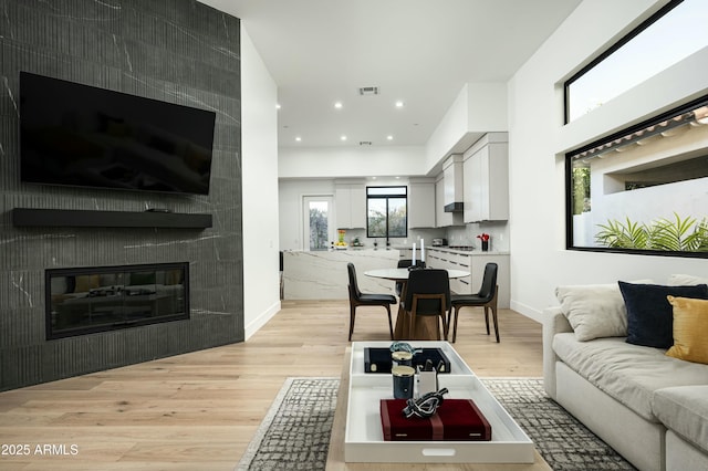 living area with a fireplace, light wood finished floors, recessed lighting, visible vents, and baseboards