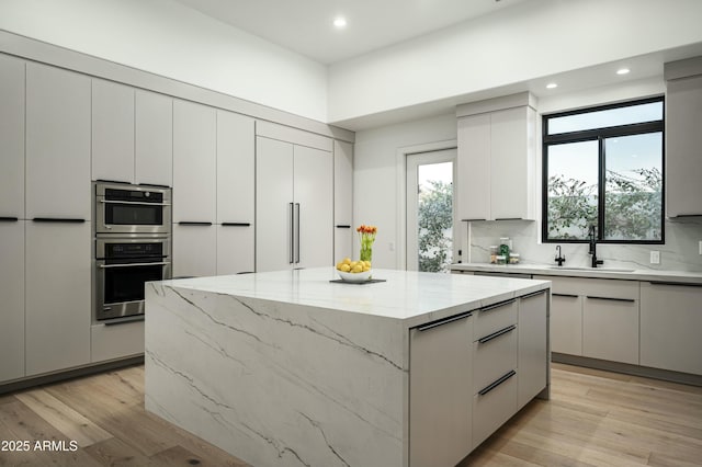 kitchen with a kitchen island, a sink, light wood finished floors, and modern cabinets