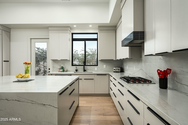 kitchen with wall chimney exhaust hood, stainless steel gas stovetop, a sink, and light stone countertops