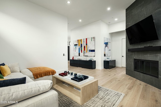 living area with recessed lighting, baseboards, a tiled fireplace, and light wood finished floors