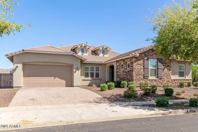 view of front of property featuring an attached garage, stone siding, decorative driveway, and stucco siding