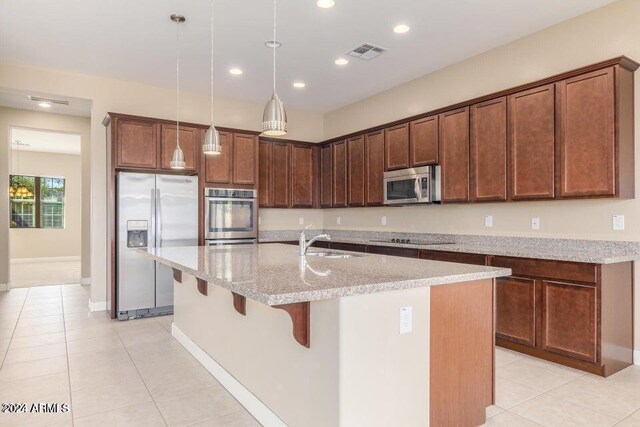 kitchen featuring a center island with sink, appliances with stainless steel finishes, sink, and light stone counters