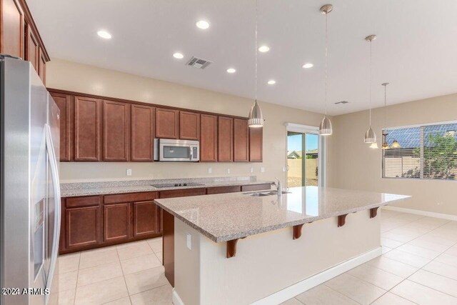 kitchen with light stone countertops, a center island with sink, sink, light tile patterned flooring, and refrigerator