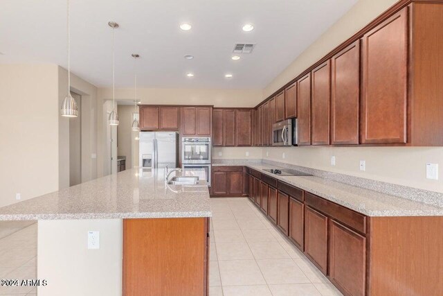 kitchen featuring stainless steel appliances, light tile patterned floors, a kitchen island with sink, light stone countertops, and sink