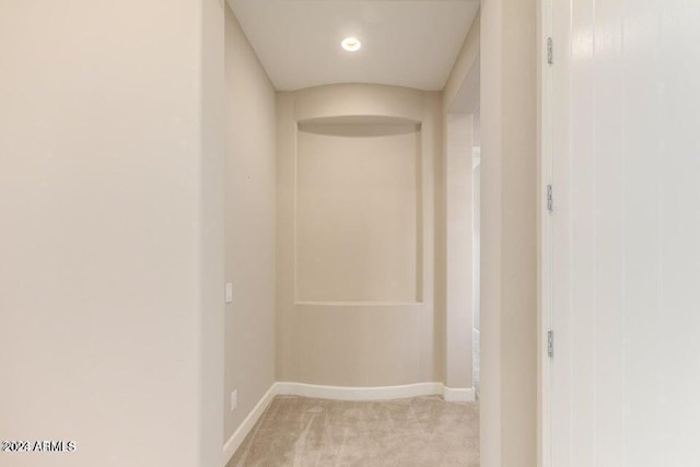 hallway with baseboards and light colored carpet