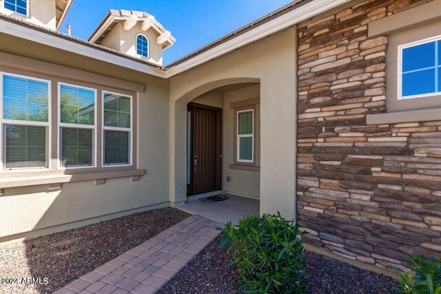 entrance to property with stone siding, a patio, and stucco siding