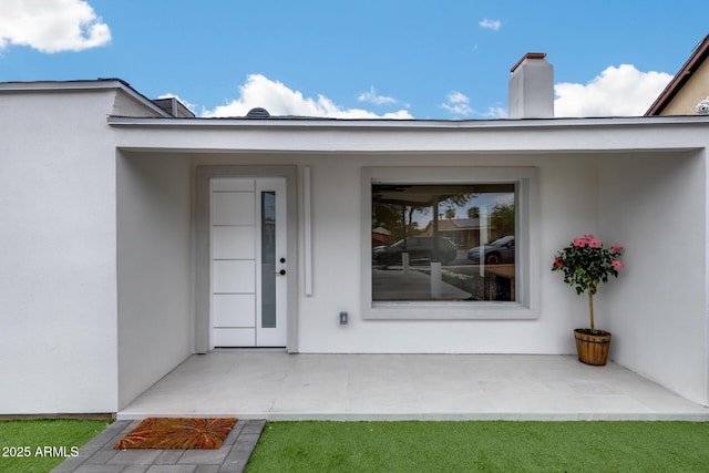 property entrance with a chimney and stucco siding