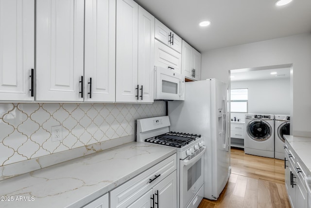 kitchen with white appliances, washing machine and dryer, light wood-style flooring, white cabinets, and decorative backsplash