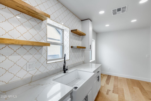 kitchen featuring light wood-type flooring, light stone counters, open shelves, visible vents, and a sink