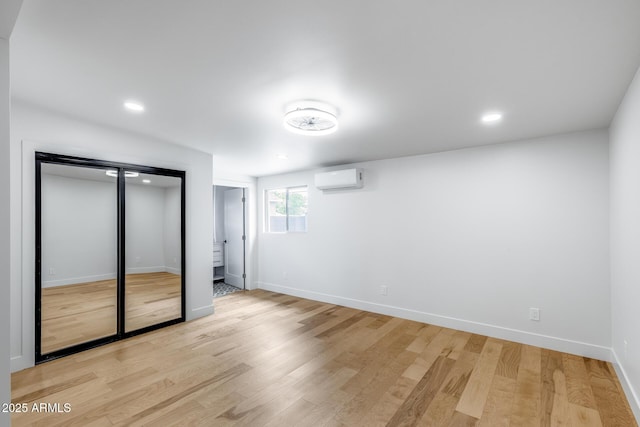 unfurnished bedroom with baseboards, light wood finished floors, recessed lighting, and a wall mounted air conditioner