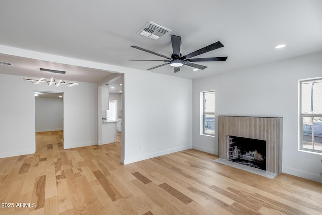 unfurnished living room featuring visible vents, light wood-style flooring, a ceiling fan, and a fireplace with flush hearth