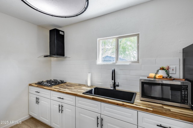 kitchen featuring stainless steel microwave, black gas cooktop, wooden counters, a sink, and ventilation hood