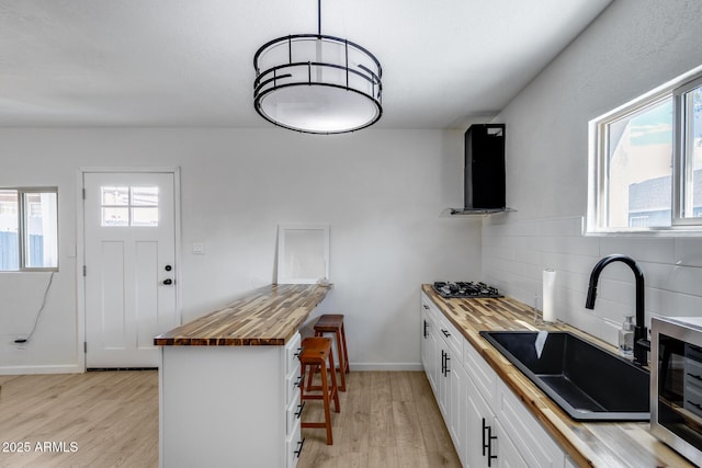 kitchen with a sink, butcher block countertops, stainless steel microwave, and light wood-style floors