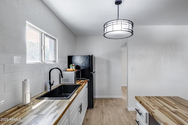 kitchen featuring light wood-style floors, butcher block counters, white cabinets, a sink, and decorative backsplash
