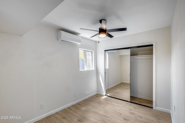 unfurnished bedroom featuring light wood finished floors, a closet, a wall mounted air conditioner, and baseboards