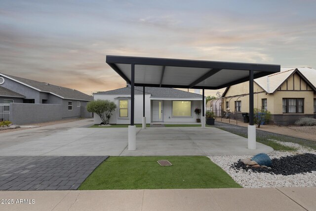 view of front facade featuring roof with shingles, driveway, stucco siding, and fence