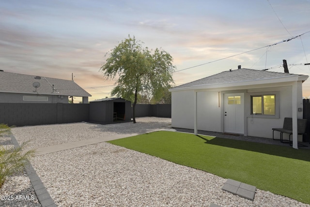 yard at dusk with a patio, an outbuilding, a fenced backyard, and a shed