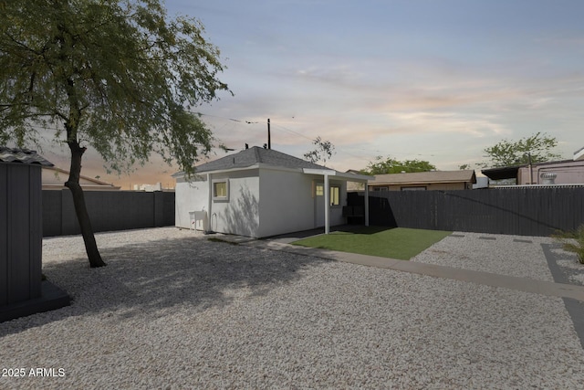 back of house at dusk featuring a patio area, a fenced backyard, gravel driveway, and stucco siding