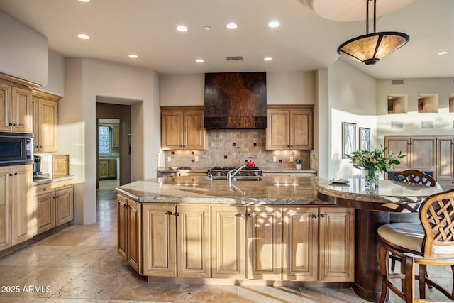 kitchen featuring hanging light fixtures, a spacious island, stainless steel microwave, light stone counters, and custom exhaust hood