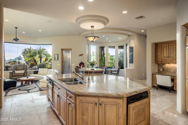 kitchen featuring sink, hanging light fixtures, light stone countertops, a kitchen island with sink, and backsplash