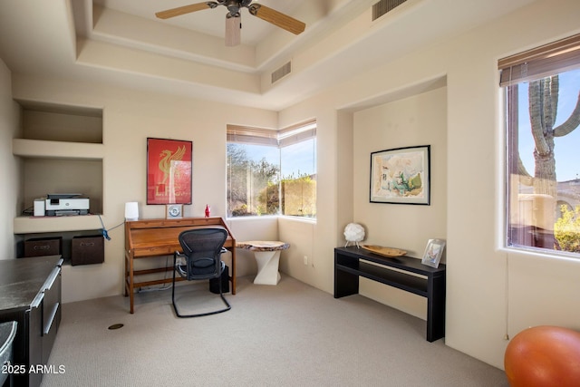 carpeted home office with a raised ceiling and ceiling fan