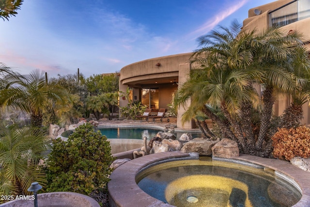 pool at dusk featuring an in ground hot tub and a patio