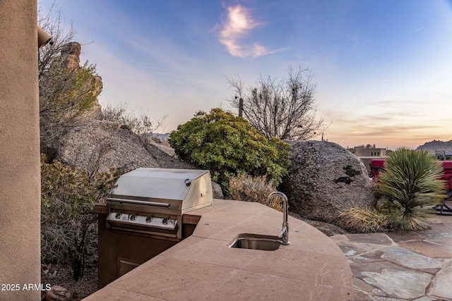 patio terrace at dusk featuring a grill and exterior kitchen