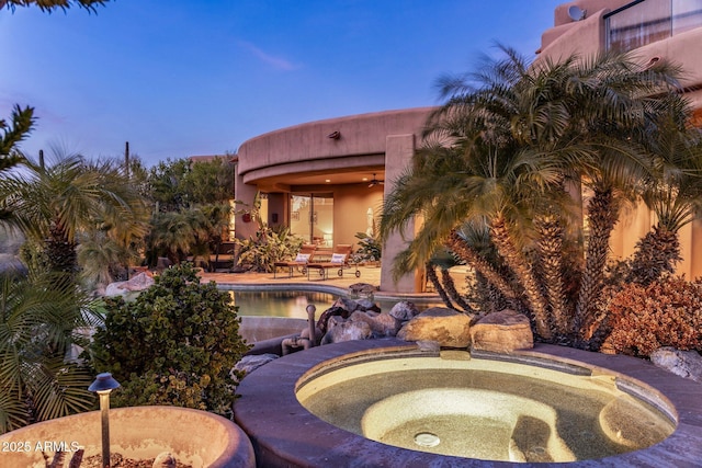 pool at dusk featuring an in ground hot tub and a patio