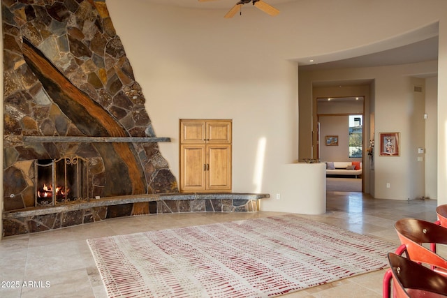 tiled living room featuring ceiling fan, a stone fireplace, and a high ceiling