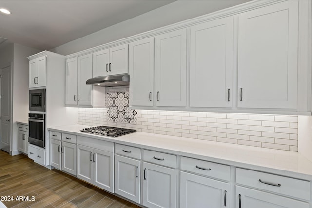 kitchen with tasteful backsplash, white cabinets, appliances with stainless steel finishes, and hardwood / wood-style floors