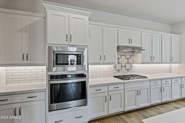 kitchen with white cabinets, stainless steel appliances, backsplash, and light hardwood / wood-style floors