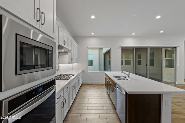 kitchen with white cabinets, sink, a center island with sink, appliances with stainless steel finishes, and light wood-type flooring