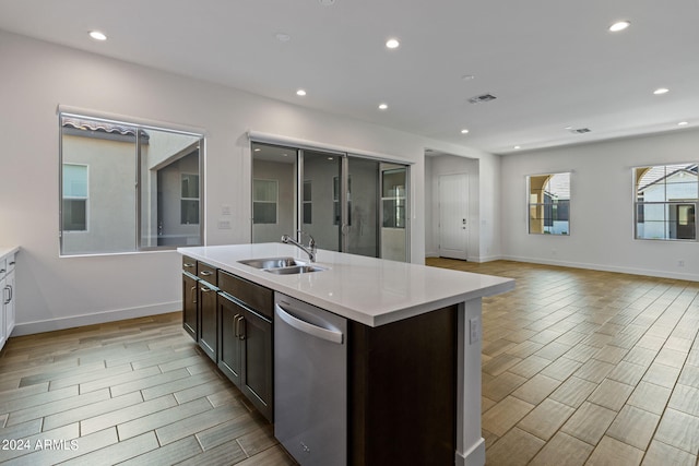 kitchen with dark brown cabinetry, stainless steel dishwasher, sink, light hardwood / wood-style floors, and a center island with sink