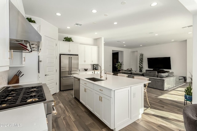 kitchen with wall chimney exhaust hood, stainless steel appliances, a kitchen island with sink, sink, and white cabinetry