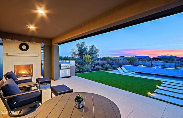 patio terrace at dusk featuring exterior kitchen, a tile fireplace, and area for grilling