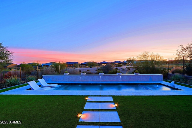 pool at dusk with a patio area and a lawn